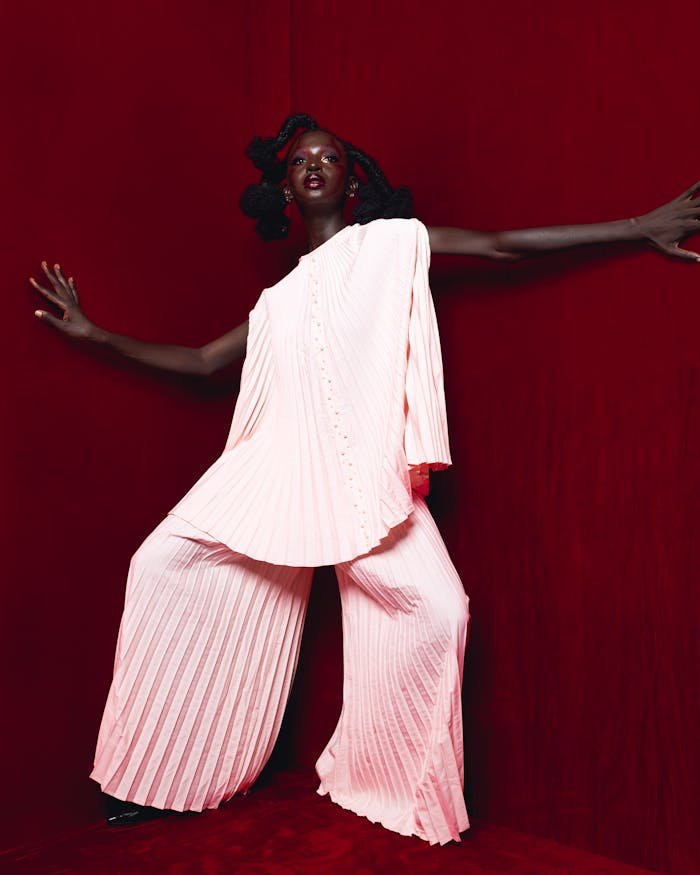 Dynamic portrait of a model in a pleated pink outfit against a rich red background.