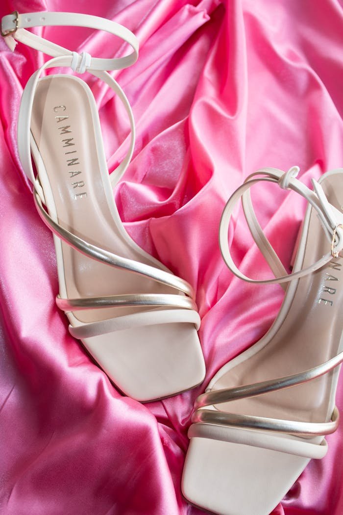Elegant beige strappy sandals placed artistically on luxurious pink satin fabric, creating a romantic and stylish look.