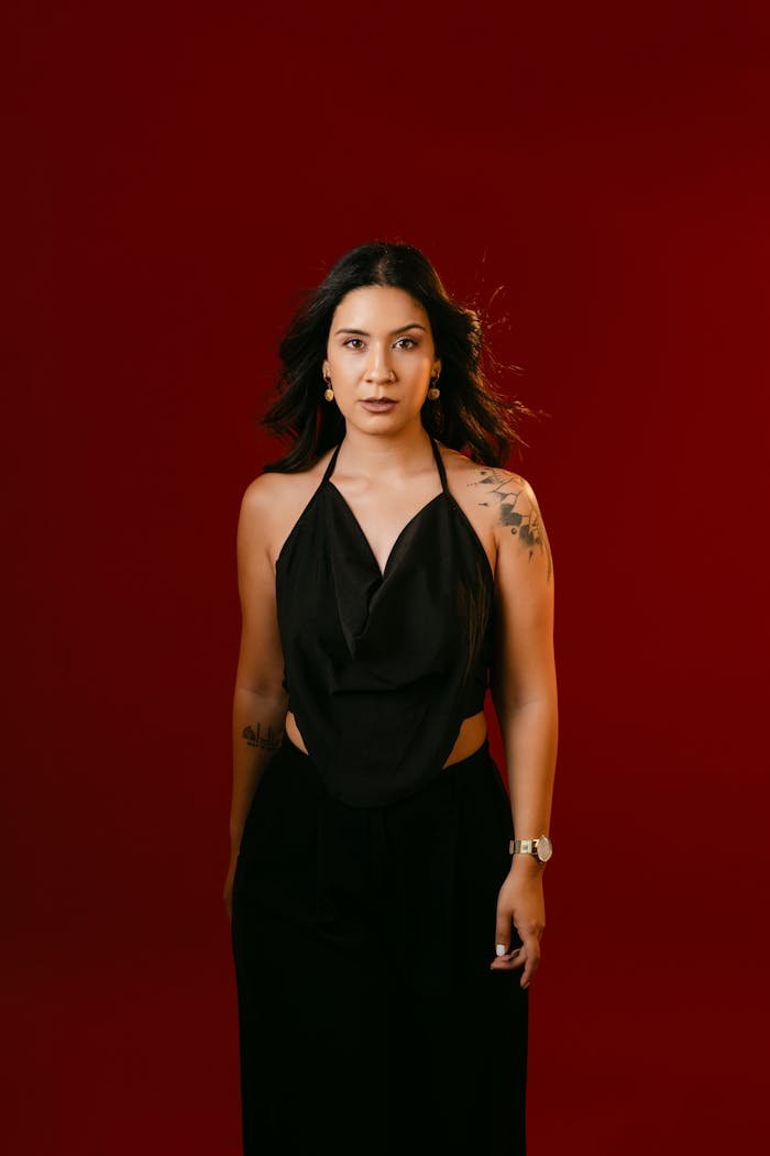Portrait of a stylish woman in a black dress against a deep red backdrop.