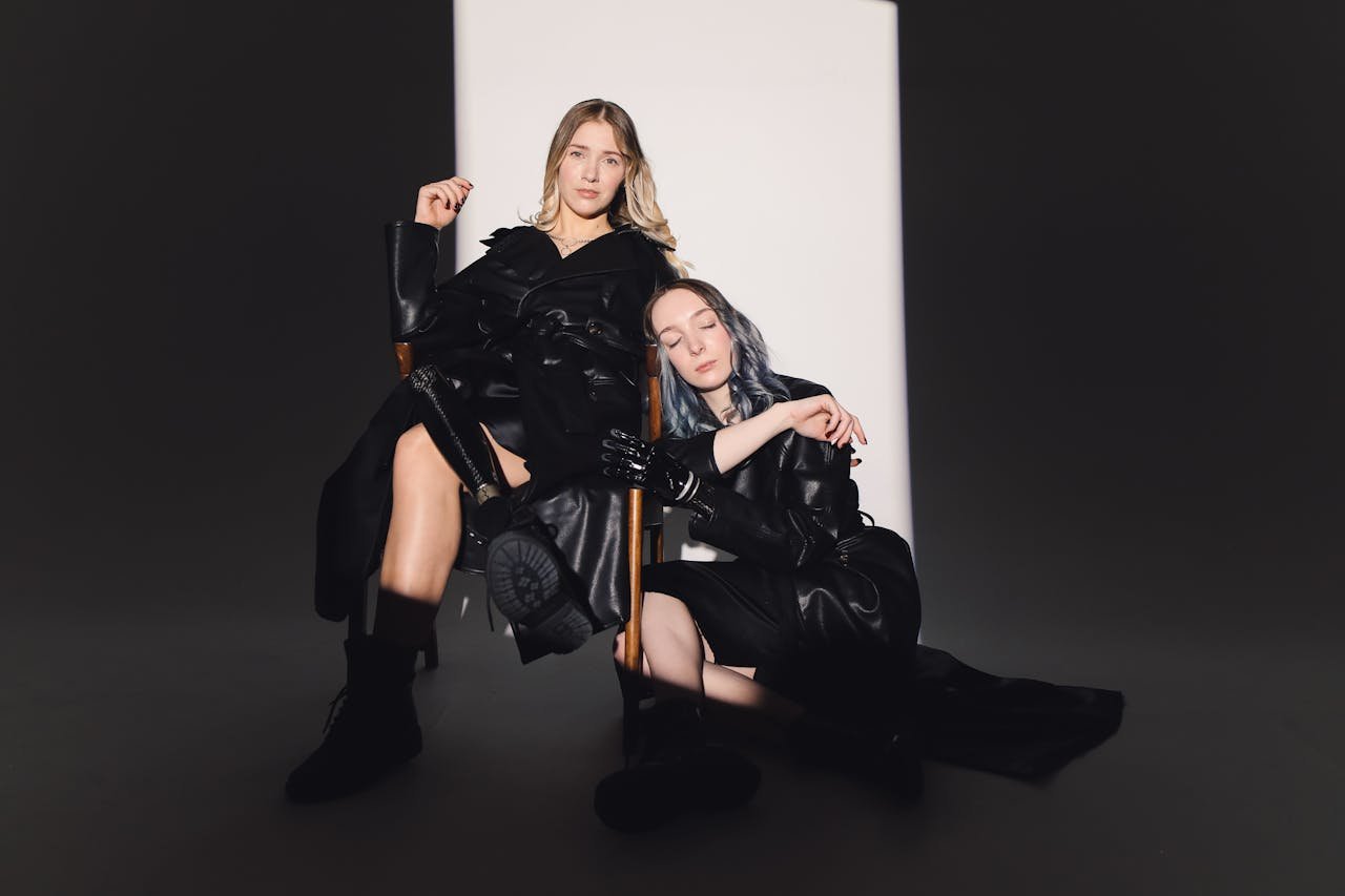 Two fashion models posing in stylish black attire under a dramatic spotlight.