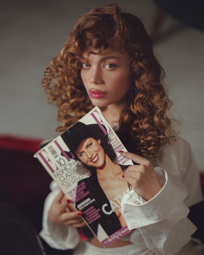 Stylish young woman holding a fashion magazine indoors, showcasing a trendy fashion concept.